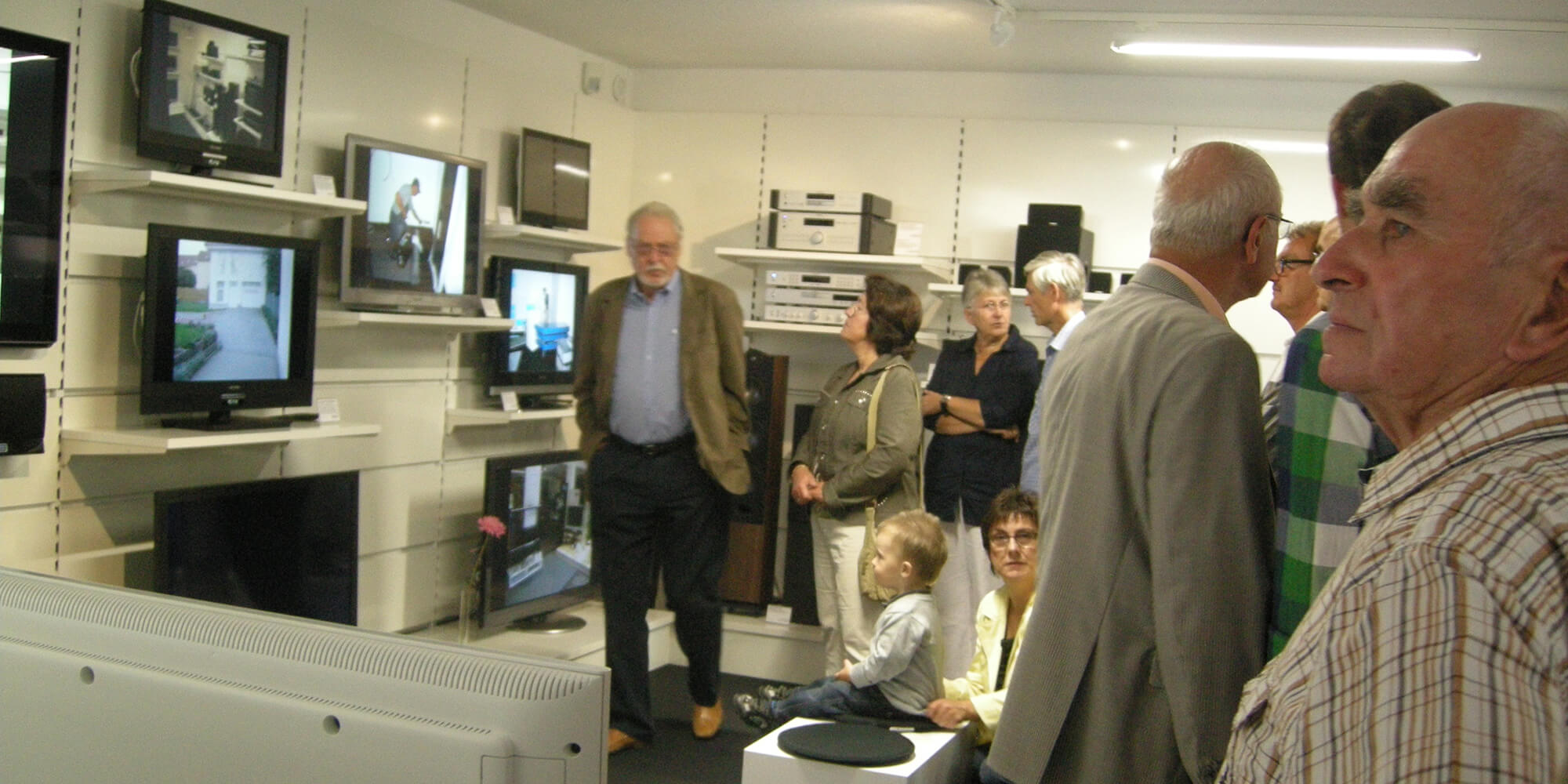 Menschen in unseren Elektronikgeschäft betrachten ausgestellte Fernseher und Audiogeräte.